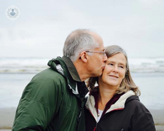Older man kissing older woman on the cheek on the beach.