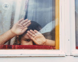 Child looking out the window with his hands on the glass