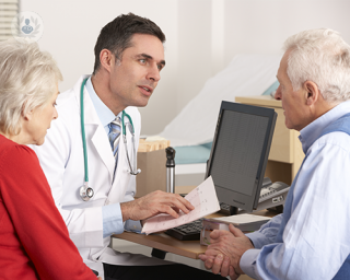 A doctor is having a consultation with an elderly patient and his partner. He is reading the results of an examination, perhaps a FibroScan.