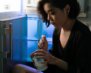 A woman sat by the fridge binging on ice cream 