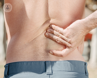 A shirtless man touching his lower back due to feeling pain