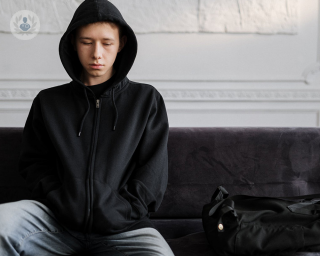Boy with chronic pain at a psychology appointment, wearing a black hoodie sat on a sofa looking sad