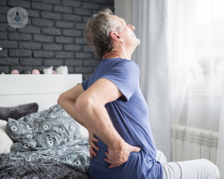 Elderly man sitting on his bed and holding his lower back in pain