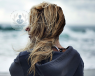 Blonde haired woman stood by the sea with back to camera, windy