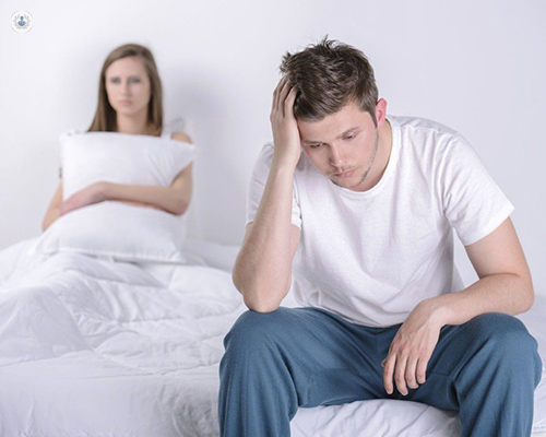 Man with erectile dysfunction looking upset while sat on bed and his partner looking annoyed