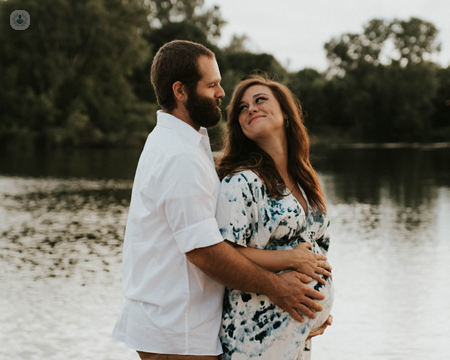 Excited pregnant couple stood by a lake, who need preconception care