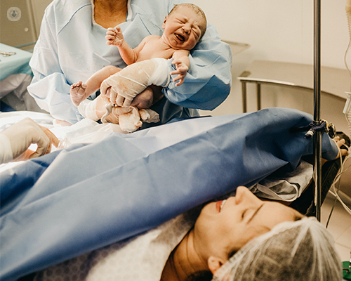 A surgeon holding a newborn baby from a caesarean section and showing the baby to its mother