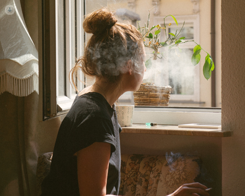 Woman smoking by a window, surrounded by smoke - a major cause of lung cancer