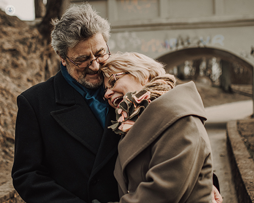 An elderly couple laughing and hugging while outdoors.