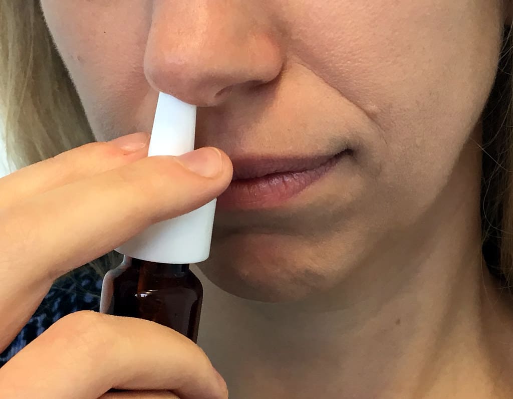 Woman uses nasal spray to alleviate hay fever.