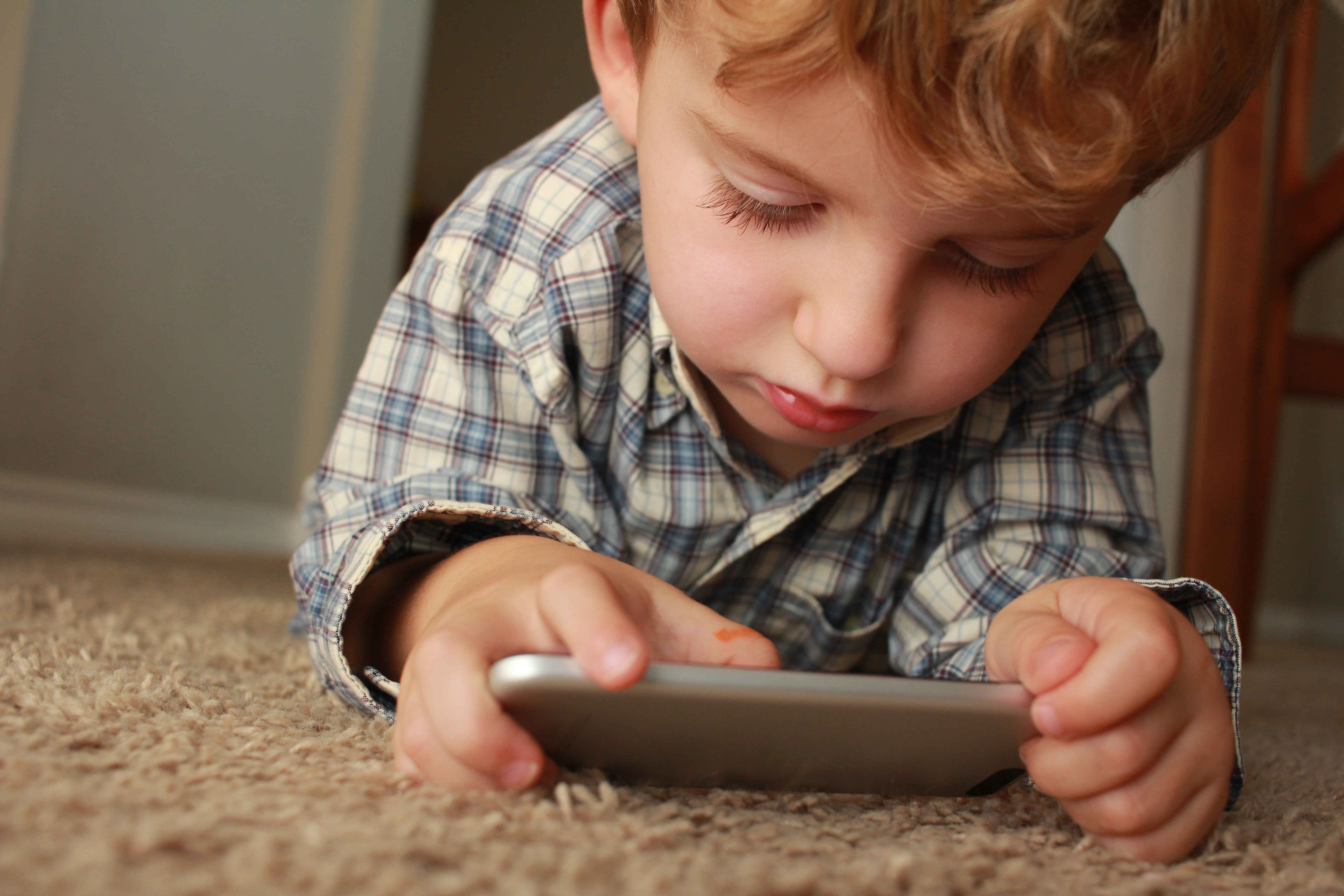 Young boy laid on the floor and playing with a mobile phone