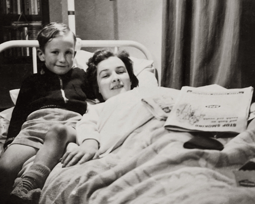 World Health Day 2023: Black and white photo from the 1950s of 60s, of a smiling young girl recovering in a hospital bed while her brother sits next to her on the bed.