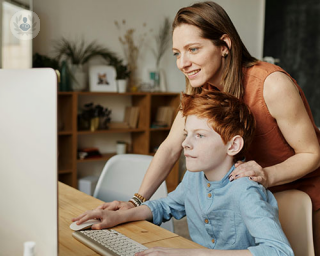 A mother at a desk looking at a computer which shows her son's homework.