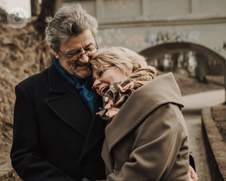 An elderly couple laughing and hugging while outdoors.