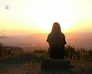A woman suffering with heartburn looking at the sunset