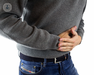 Man wearing grey jumper and blue jeans holding onto stomach