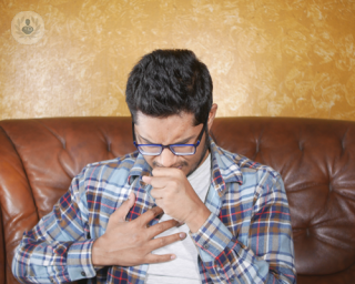 Young man with a chronic cough sat down on a brown sofa indoors