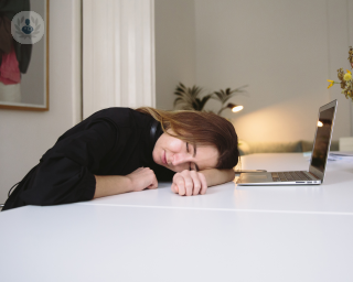 Woman sleeping with her head on a table next to her laptop