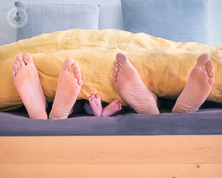 Two adults and a child laying in bed, showing only their feet at the end of the bed