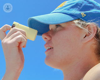 A teenage boy with a cap putting sunscreen on his nose.