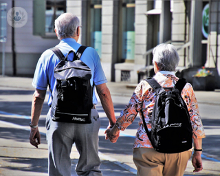 A man and woman shown from behind holding hands whilst walking around town.
