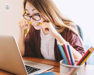 A woman is working on her laptop looking anxious and chewing a pencil. The Covid-19 crisis is causing many people to have anxiety about it.