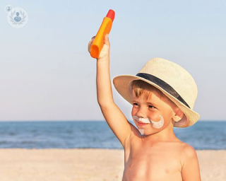 young child on the beach with a sun hat and holding sun cream