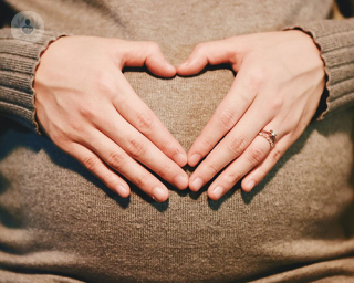 woman with hands in shape of a heart over her pregnant stomach