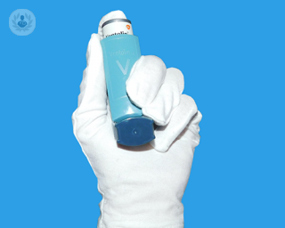 A gloved hand holding a Ventolin asthma inhaler.