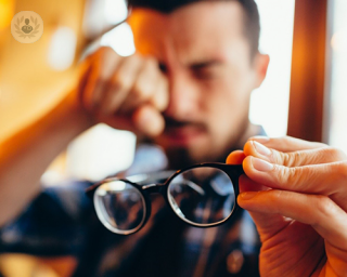 Man rubbing his eye and holding his glasses