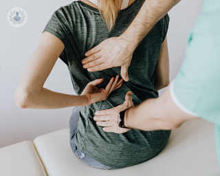 A woman experiencing back pain at a consultation, where a doctor is performing a physical examination. 