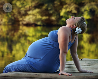 A pregnant woman resting on a pier overlooking a lake.