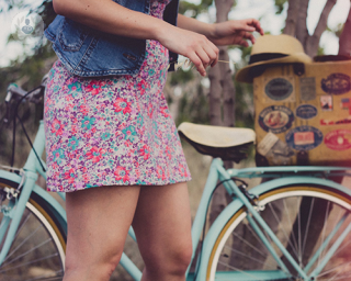 Side image of a girl's legs. The girl is wearing a flowery dress as she goes to grab her bike.
