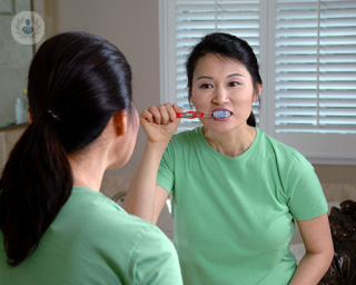 asian woman brushing teeth in mirror