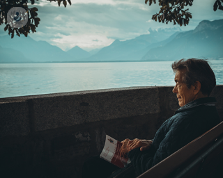 Old man looking out over water reading book