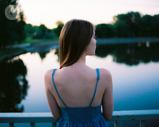 A woman standing in front of a pond with her back to the camera.