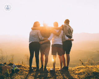Group of friends hugging and watching a sunset over mountains