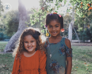 Two little girls smiling at the camera, stood in a sunny garden