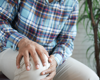 An adult man clutching his right knee with his both hands, feeling knee pain.