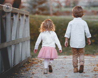 A boy and girl walking away from the camera. The boy is taller than the girl.