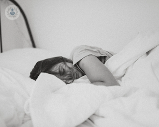 A black and white image of a woman sleeping in bed. 