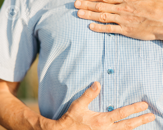 A man holding a hand to his chest and a hand to his stomach, as a result of heartburn and stomach pain.