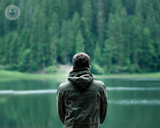 A man standing, looking out into the lake and forest in front of him.