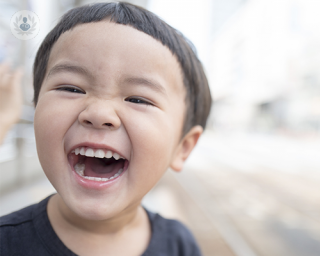 A young boy of around five years old is looking into the camera. He is smiling, laughing and showing his teeth
