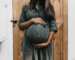 A pregnant woman stands showing her belly.