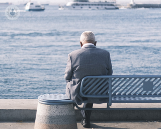 An elderly man sat on a bench in front of the sea, contemplating.