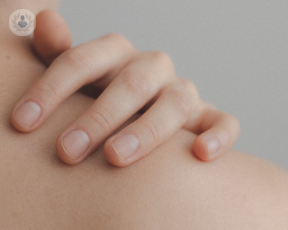 A close up of a person's bare skin between the neck and shoulder. A person's hand is resting on it.