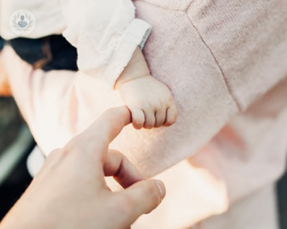 A baby holding their mother's index finger. Some babies are born with congenital heart disease.
