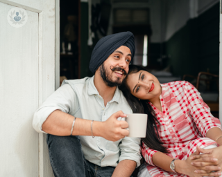 Happy Sikh couple sat in the doorway of a house, with the ladies head resting on her partner's shoulder