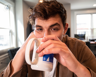 A young man looking tired while drinking a cup of coffee.